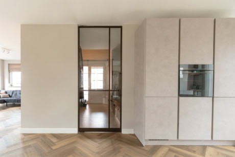 Strakke stalen deur met glazen panelen tussen keuken en woonkamer, modern interieur, natuurlijke lichtinval, hoogwaardige afwerking, geschikt voor maatwerk stalen deuren.