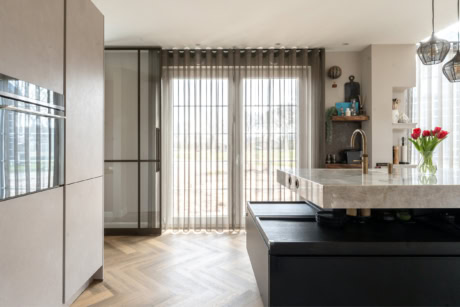 Moderne stalen schuifdeur in keuken met grote ramen en lichte gordijnen, natuurlijke lichtinval, strakke afwerking, en een stijlvolle keuken met bloemen en accessoires.