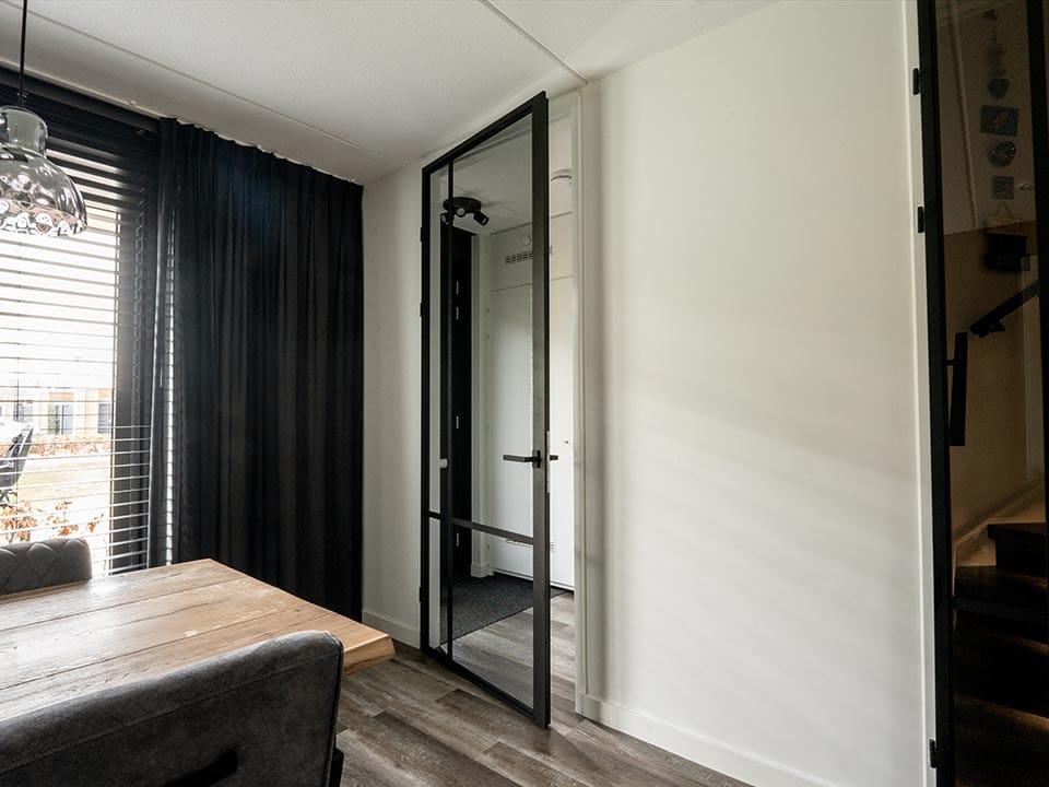 Moderne stalen schuifdeur met glas in een eigentijdse woonkamer, ideaal voor scheiding van ruimtes en designaccent.