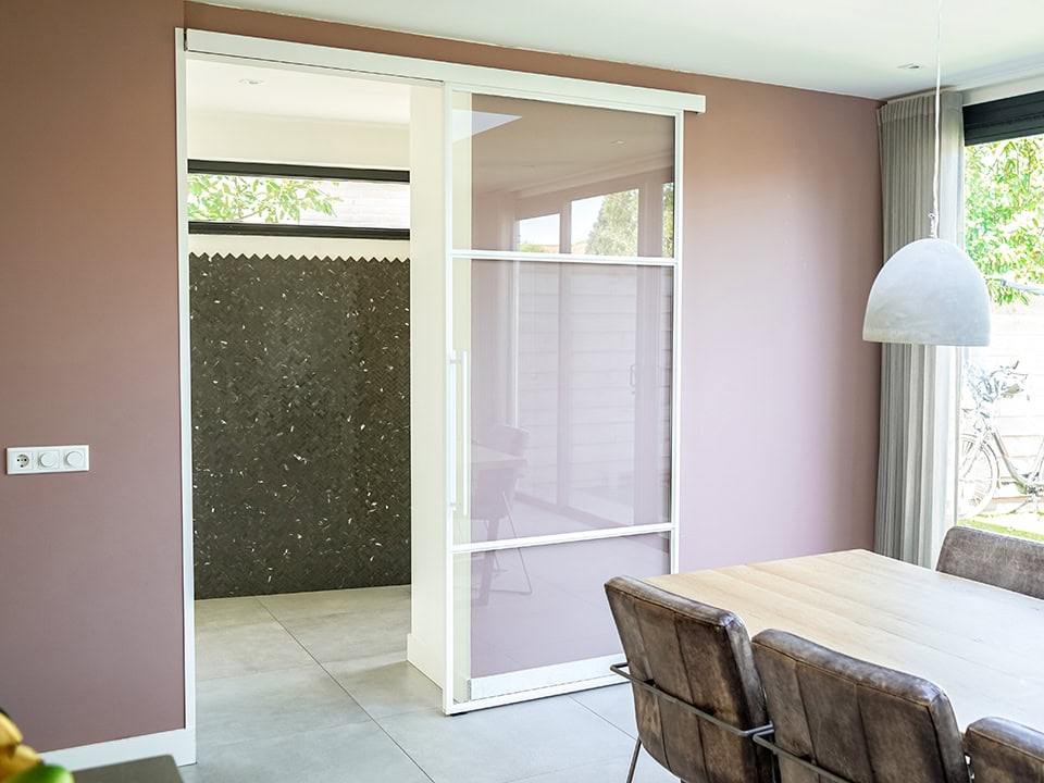 Moderne stalen schuifdeur met glas in woonkamer, scheidt de eetkamer van de buitenruimte, met natuurlijke lichtinval en strakke afwerking.