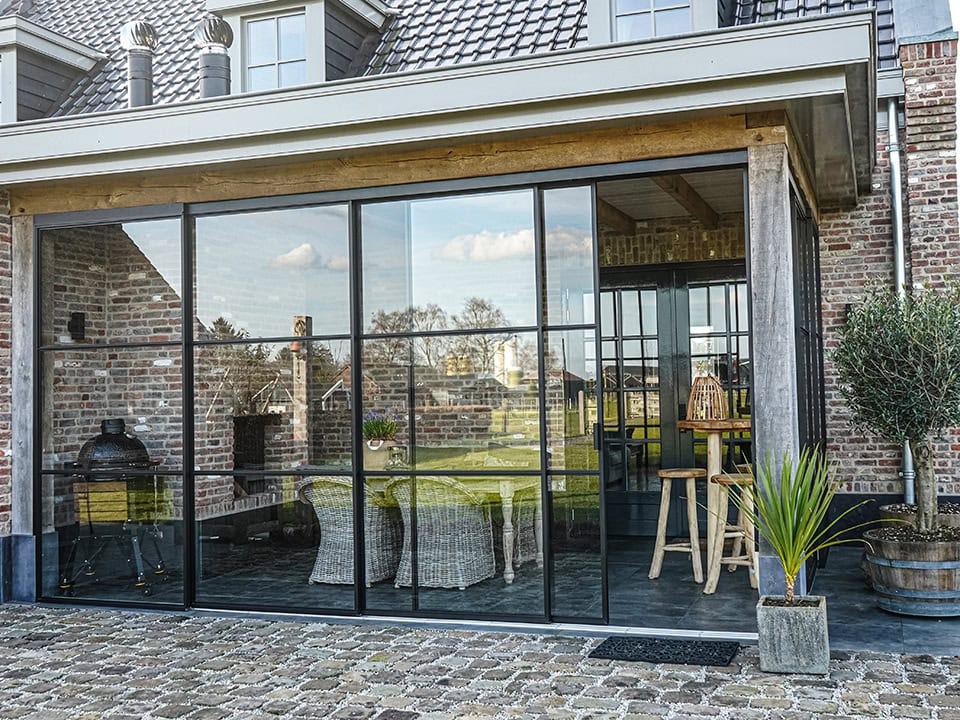 Moderne aluminium terrasoverkapping met grote glazen wanden en uitzicht op tuin, ideaal voor buitenleven en bescherming tegen weer.