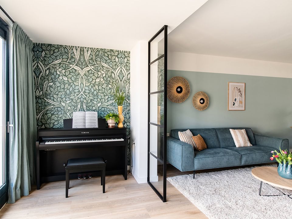 Lichte woonkamer met stalen room divider, bank, muurdecoraties en piano, stijlvolle interieurindeling voor Crittall room dividers.