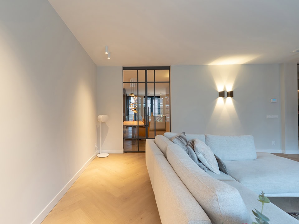 Strakke stalen schuifdeur met glazen panelen in een moderne woonkamer, ideaal voor scheiding van ruimtes en designaccent.
