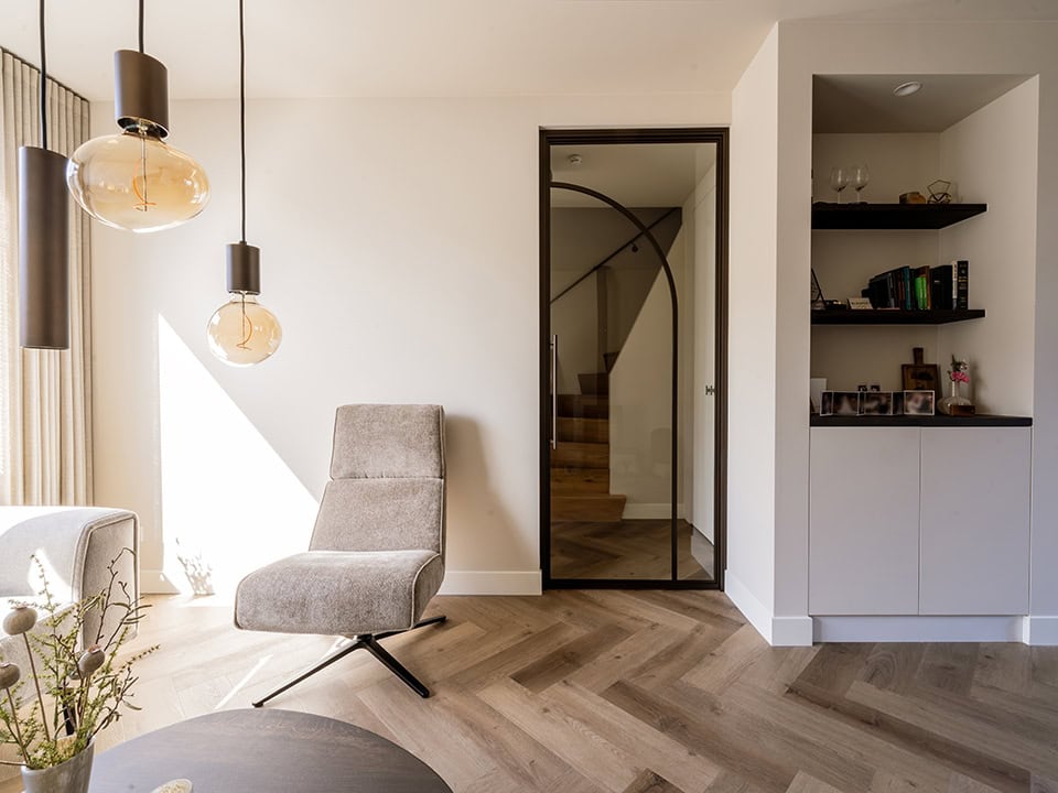 Binnenruimte met moderne stalen deur, comfortabele stoel, en natuurlijke lichtinval, passend bij hoogwaardige stalen deuren en wanden op maat.