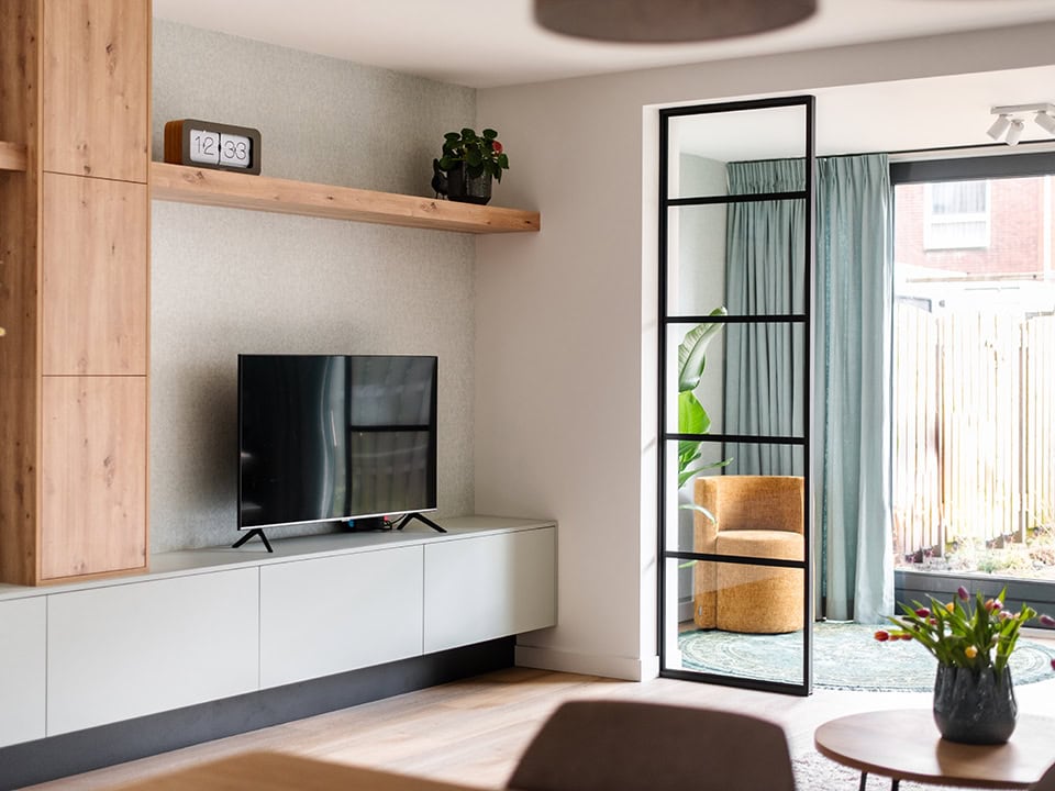 Strakke zwarte stalen deur met glas in woonkamer, scheidt binnenruimte van tuin, modern interieur, natuurlijke lichtinval, stijlvolle woningdecoratie.