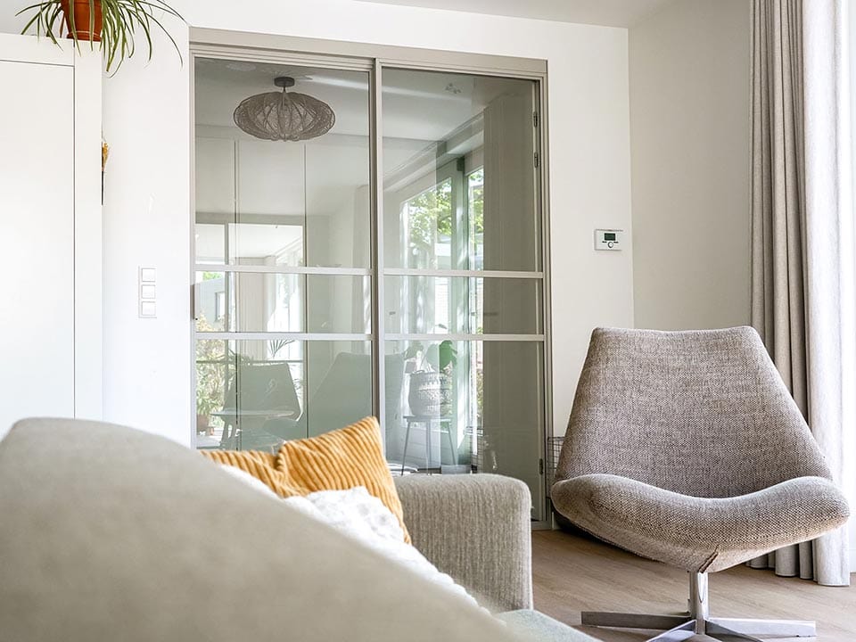Moderne stalen schuifdeur met glazen panelen in een eigentijdse woonkamer, ideaal voor scheiding van ruimtes en lichtdoorlatendheid.