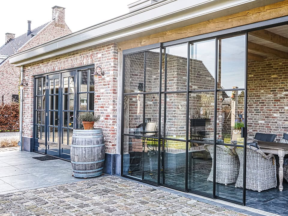 Moderne stalen schuifdeuren met grote glazen panelen voor een strakke uitstraling en optimale lichtinval, perfect voor buiten- en binnenruimtes.