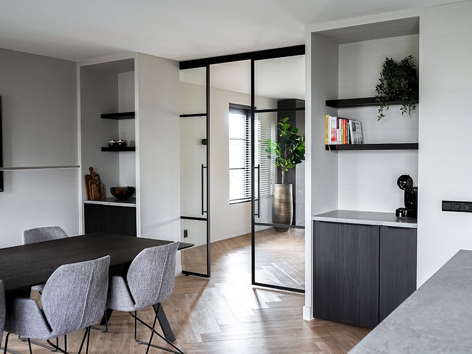 Elegante stalen scheidingswand met glazen panelen in een modern interieur, scheidt de woonkamer van de eetkamer en creëert een open, lichte ruimte.