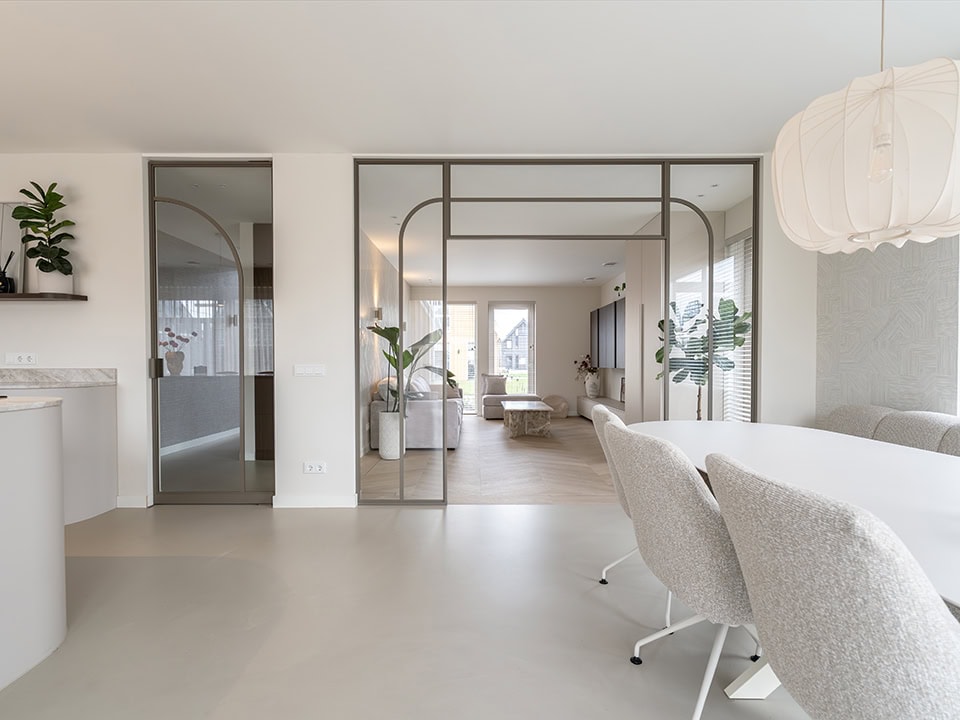 Lichte, moderne woonkamer met stalen scheidingswand en deur, grote ramen en minimalistisch interieur, geschikt voor stijlvolle woningindeling.