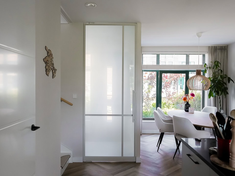 Moderne witte stalen deur op maat, scheidt de woonkamer van de eetkamer, met grote ramen en natuurlijke lichtinval, geschikt voor hoogwaardige stalen deuren en wanden.