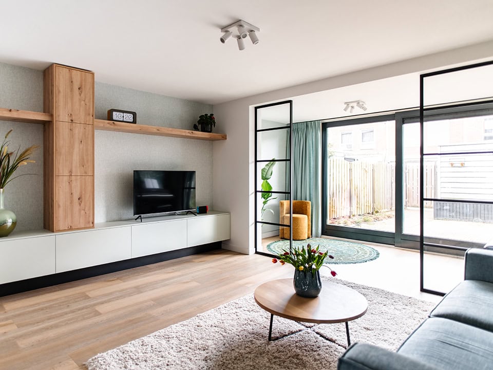 Lichte woonkamer met stalen Crittall room dividers, grote ramen, houten vloer, moderne inrichting en natuurlijke lichtinval.