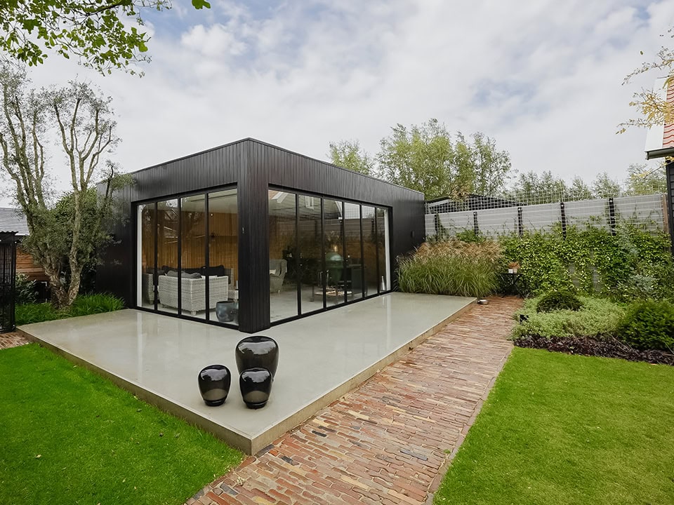 Moderne stalen tuindeur en wand op maat, perfect voor buitenruimte, met grote glazen panelen en een strakke zwarte afwerking, omgeven door groen en een tuinpad.