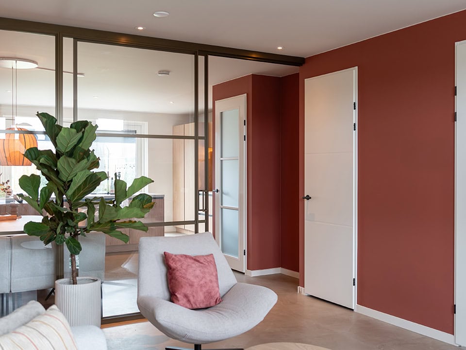 Interieur met stalen binnendeuren en een comfortabele zithoek, inclusief een plant en decoratieve kussens, in een eigentijdse woning.