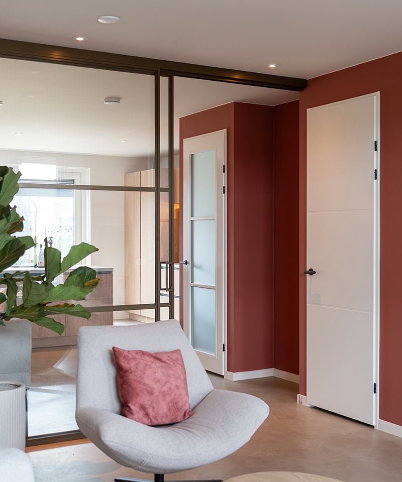 Elegante witte schuifdeuren in een modern interieur met een rood accentmuur en comfortabele zithoek met kussen, perfect voor stijlvolle woningindeling.