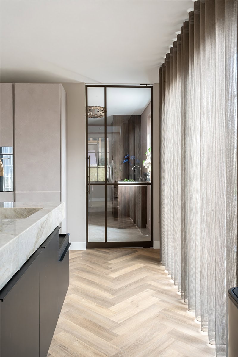 Moderne stalen pivotdeur met bronzen afwerking, perfect voor op maat gemaakte stalen deuren en wanden, in een eigentijds interieur met natuurlijke lichtinval.