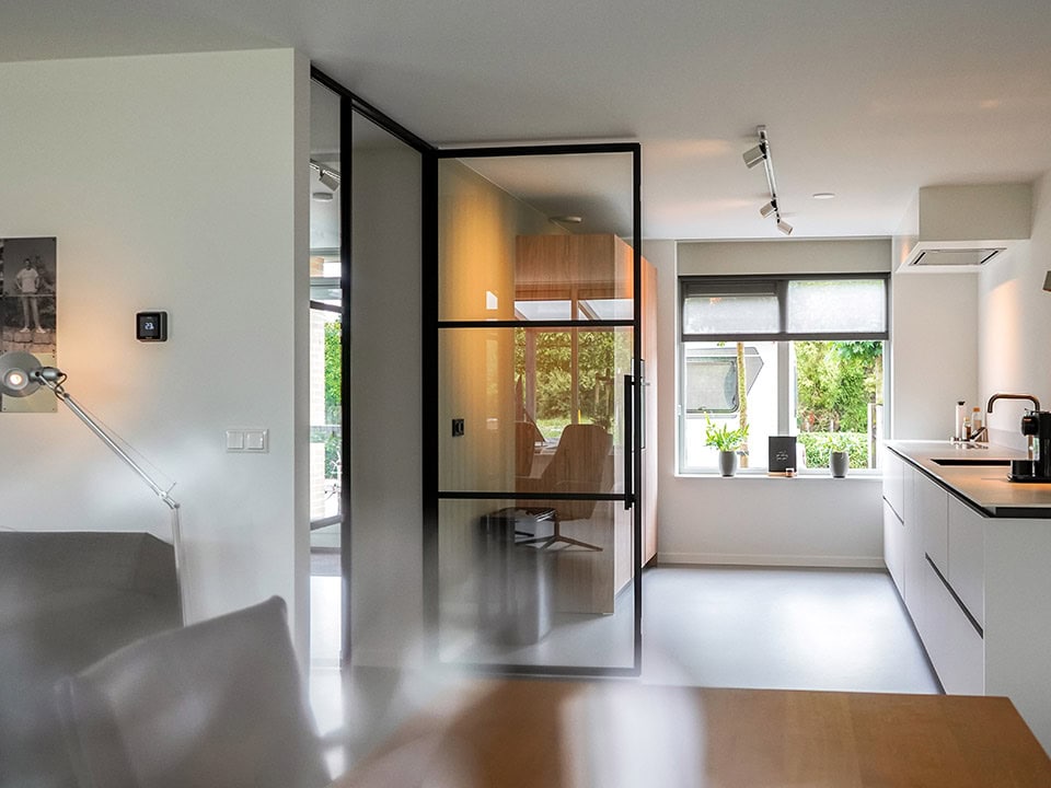 Strakke stalen deur en scheidingswand in een moderne keuken en woonkamer, op maat gemaakt voor een stijlvolle indeling en optimale ruimtegebruik.