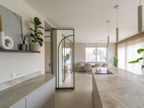 Luxe interieur met stalen scheidingswand en deur, grote ramen met gordijnen, minimalistisch design, natuurlijke lichtinval, planten en moderne meubels.