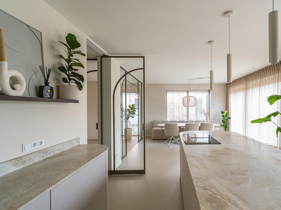 Luxe interieur met stalen scheidingswand en deur, grote ramen met gordijnen, minimalistisch design, natuurlijke lichtinval, planten en moderne meubels.