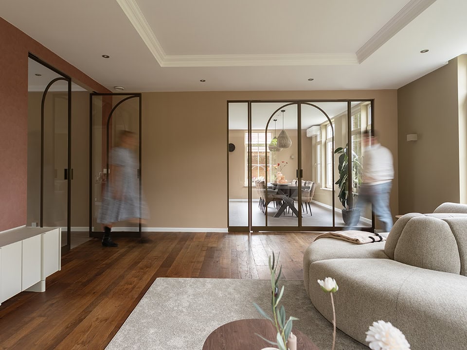 Moderne stalen scheidingswanden in een woonkamer, ontworpen voor stijlvolle indeling en privacy, met grote glazen panelen en een warme interieurstijl.