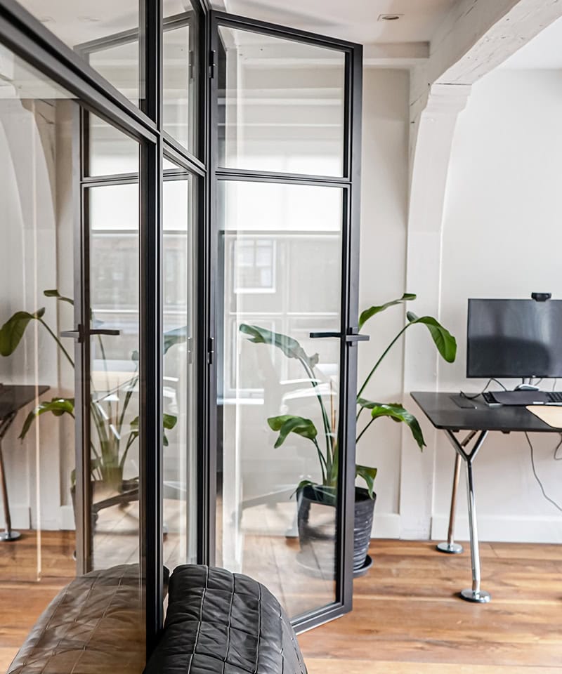 Moderne stalen deur met glas in kantoorruimte, geschikt voor scheiding en privacy, met natuurlijke lichtinval en strakke afwerking.
