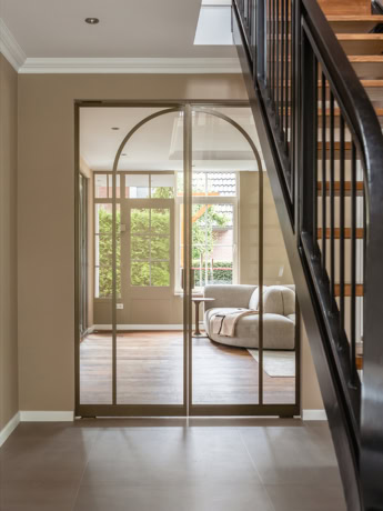 Moderne stalen schuifdeur met boogdesign en glas, scheidt de woonkamer van de hal, met natuurlijke lichtinval en een stijlvolle uitstraling.