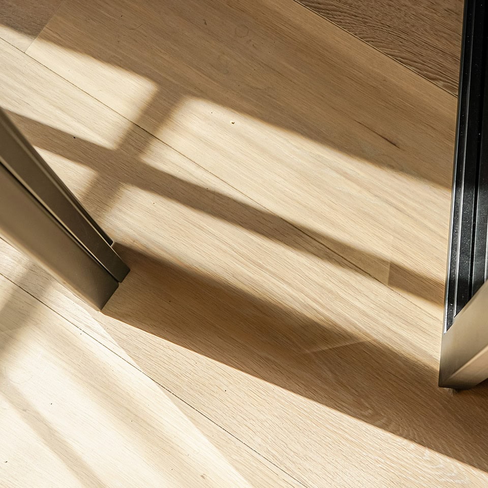 Close-up van een houten vloer en een stalen deur met zonlicht dat schaduwen werpt, geschikt voor hoogwaardige stalen deuren en wanden.