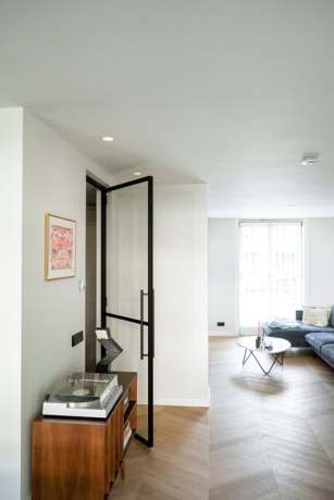 Moderne stalen schuifdeur met zwart frame in een lichte woonkamer, ideaal voor op maat gemaakte stalen deuren en wanden, passend bij Aluwdoors.