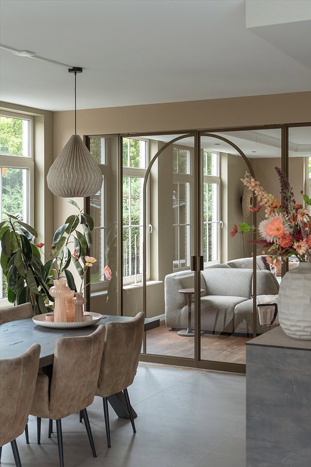 Luxe interieur met stalen deuren en grote ramen, natuurlijke lichtinval, bloemen en moderne meubels in een stijlvolle woonruimte.