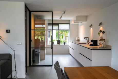 Strakke stalen scheidingsdeur in moderne keuken met grote ramen, witte kasten en minimalistisch design, perfect voor industriële en moderne interieurs.
