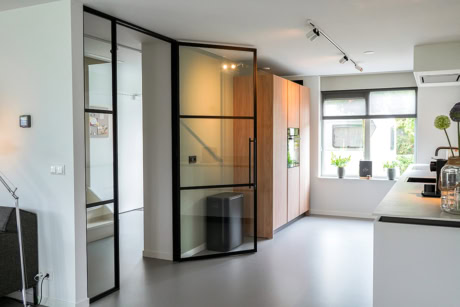 Strakke stalen deur met glazen panelen in een moderne keuken en woonkamer, perfect voor op maat gemaakte stalen deuren en wanden.