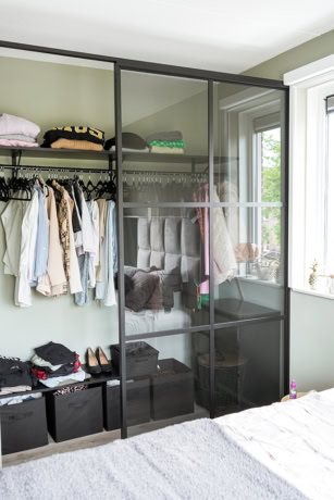 Moderne stalen schuifdeur met glazen panelen in slaapkamer, scheidt de kledingkast van de rest van de kamer, biedt een strakke en industriële uitstraling.