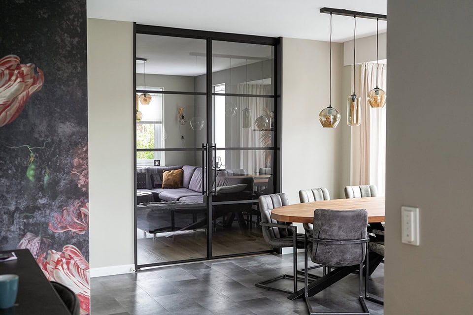 Moderne stalen schuifdeur met zwart frame, scheidt de woonkamer van de eetkamer, en voegt industriële stijl toe aan het interieur.