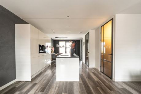 Moderne keuken met stalen deuren en witte kasten, houten vloer en grote ramen voor natuurlijk licht, passend bij hoogwaardige stalen deuren en wanden op maat.