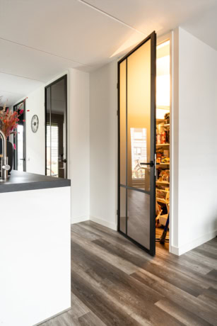 Moderne stalen deur met glas, perfect voor keuken of pantry, met een zwart frame en een warme binnenkant, in een eigentijdse woning.